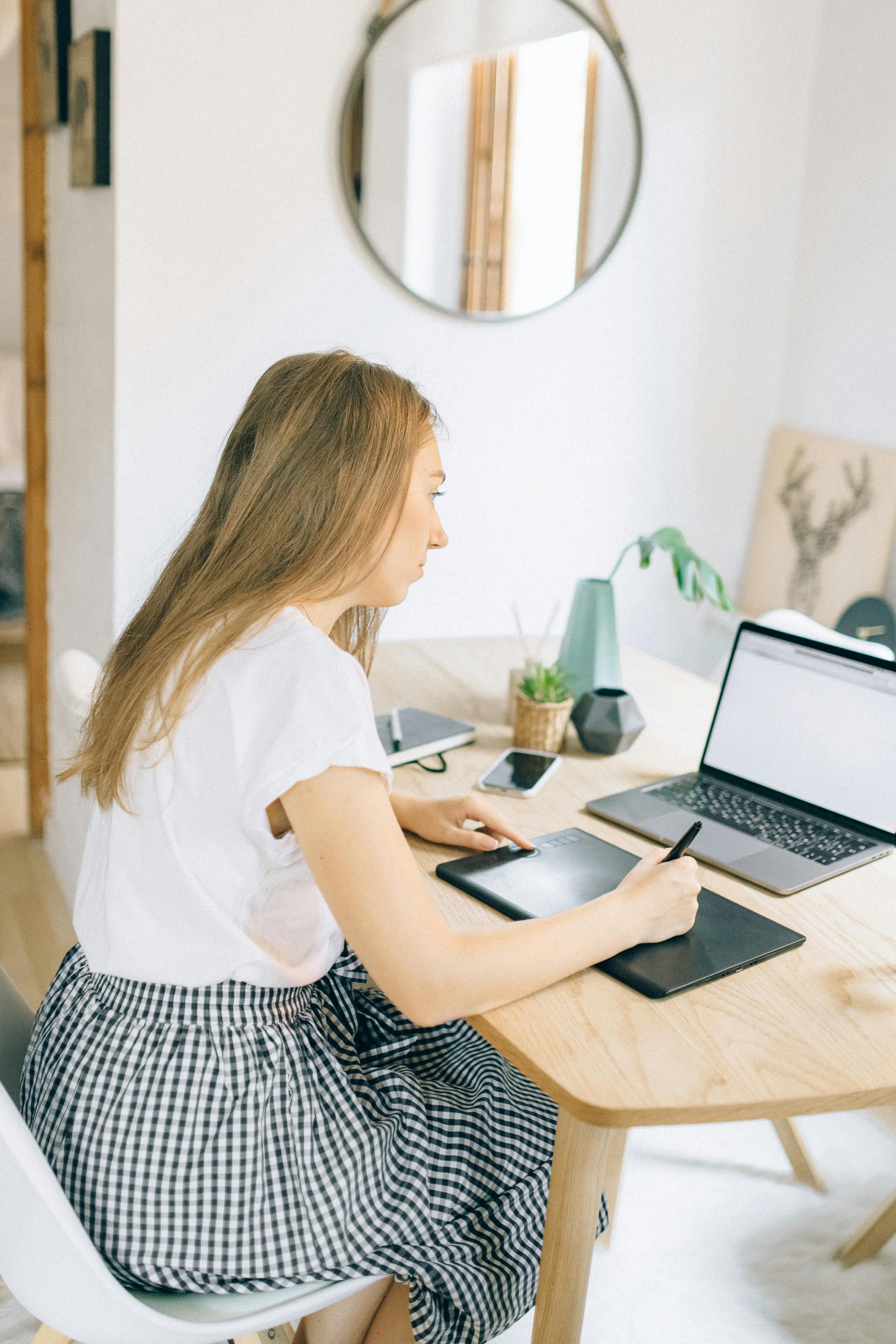 Inicio Young woman multitasking with laptop and graphic tablet in home office setting.